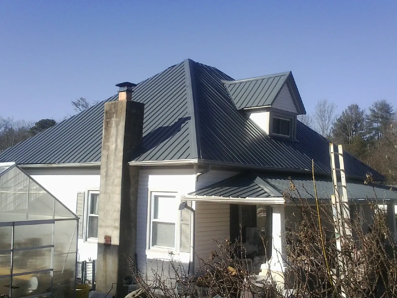 Dark blue standing seam metal roof on a white farmhouse with dormer in La Crosse