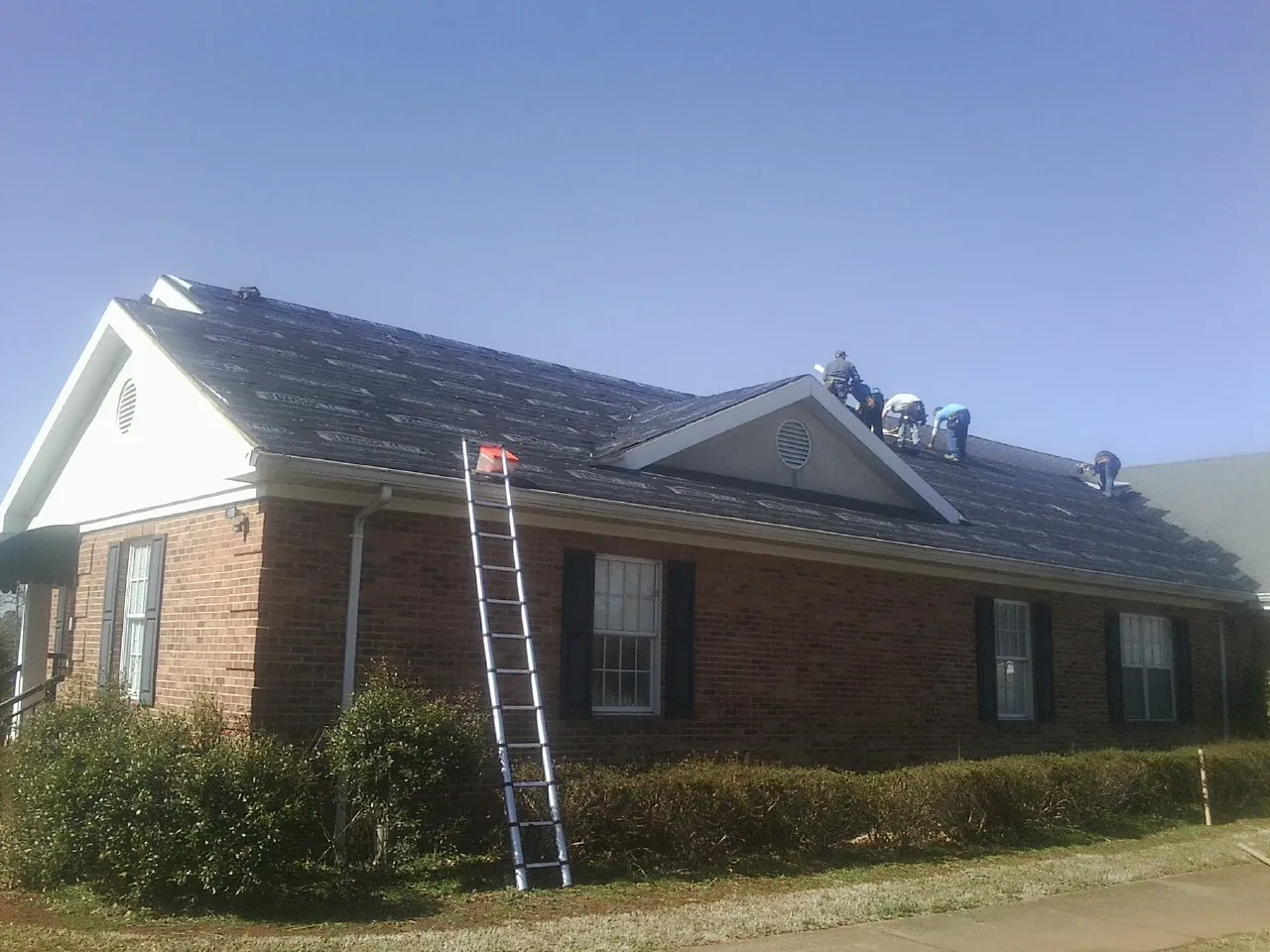 Crew tearing shingles off a brick ranch roof with a ladder set — Metal Roof Repair work by our crew in La Crosse