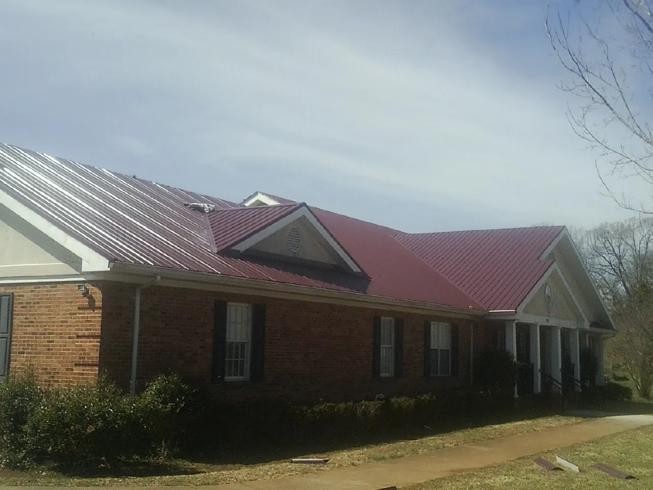 Red metal roof with gabled entries on a long brick building, from a Hail Damage Roof Repair job in La Crosse