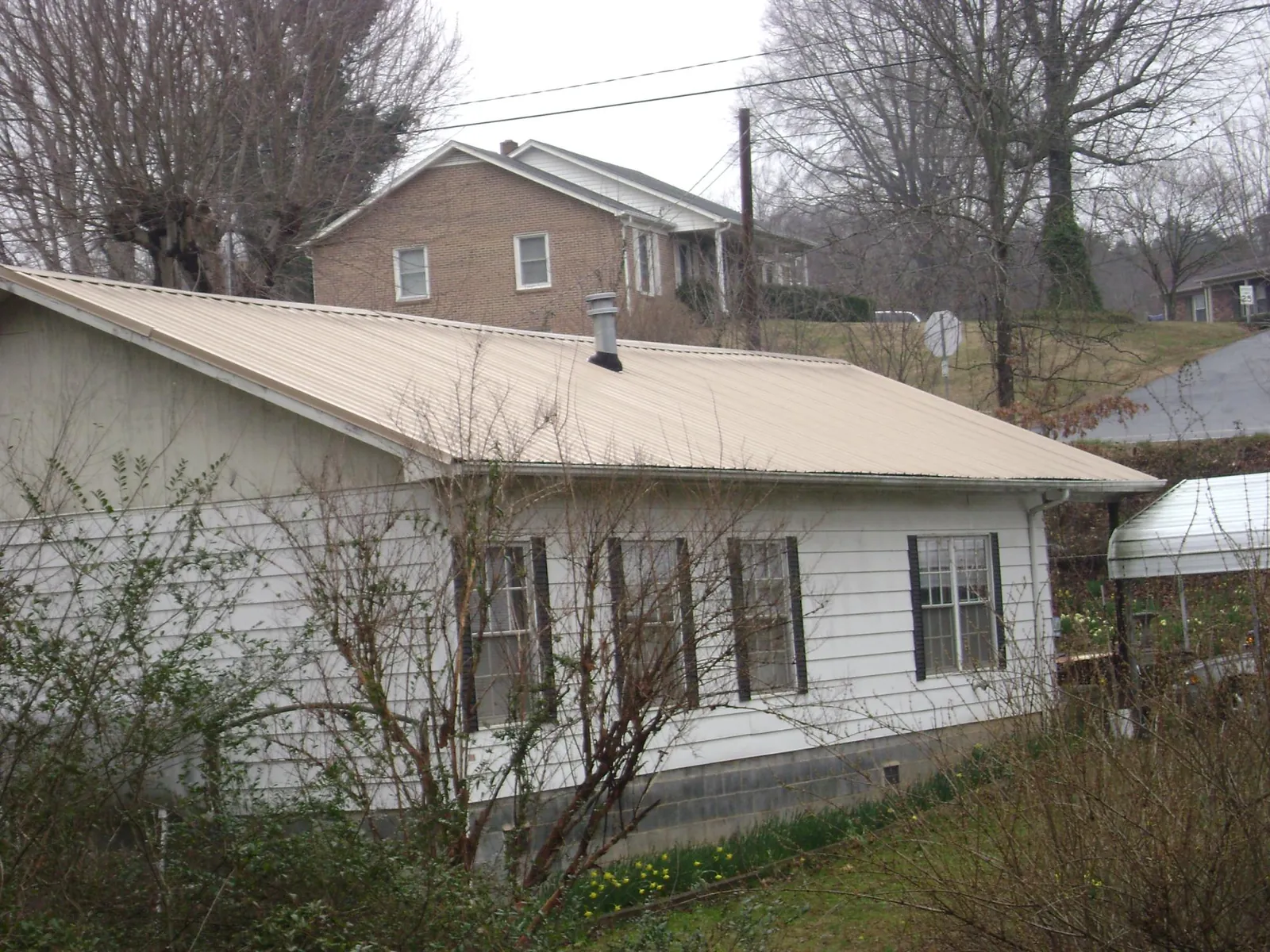 Tan metal roof on a white sided house set into a hillside — Commercial Roofing by Roofing Brothers in La Crosse